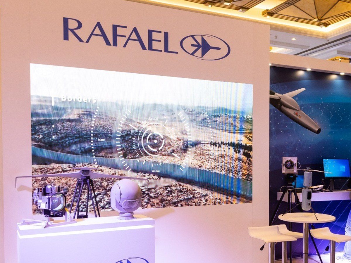 A white stand volume carrying a backlit aerial graphic, a lit counter below and a dark blue bay beyond.
