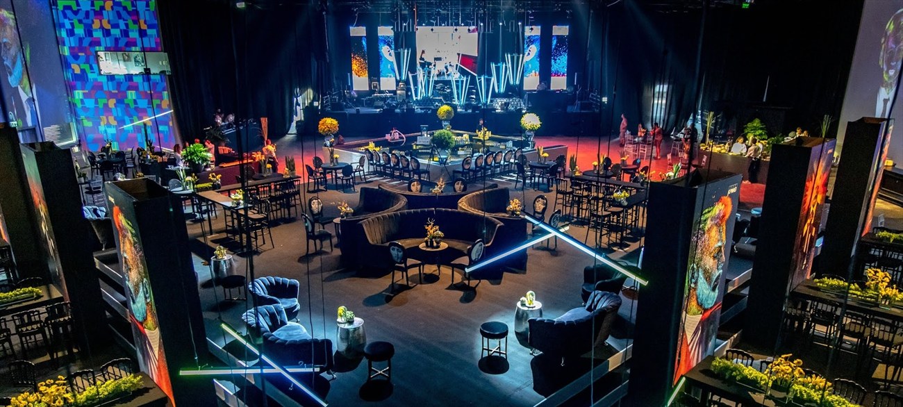A room seen from above, pale terraced seating cutting across a dark floor under lines of blue and green light.