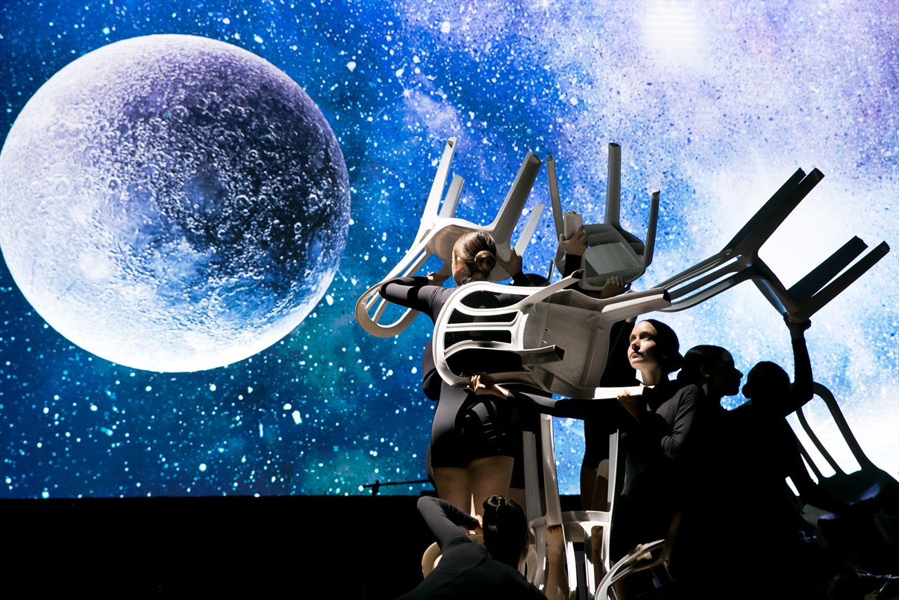 A performance on stage against a screen showing a moon.