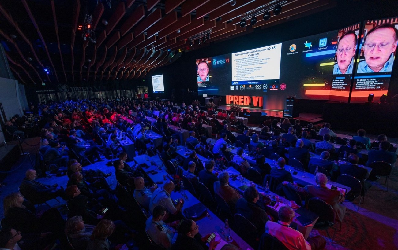 The same hall full, a speaker on stage carried on the screens.