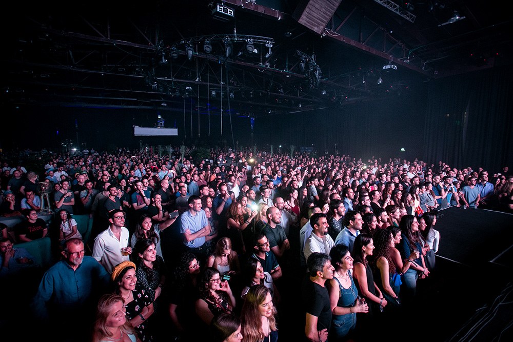 A crowd filling the room, faces lit from the stage.