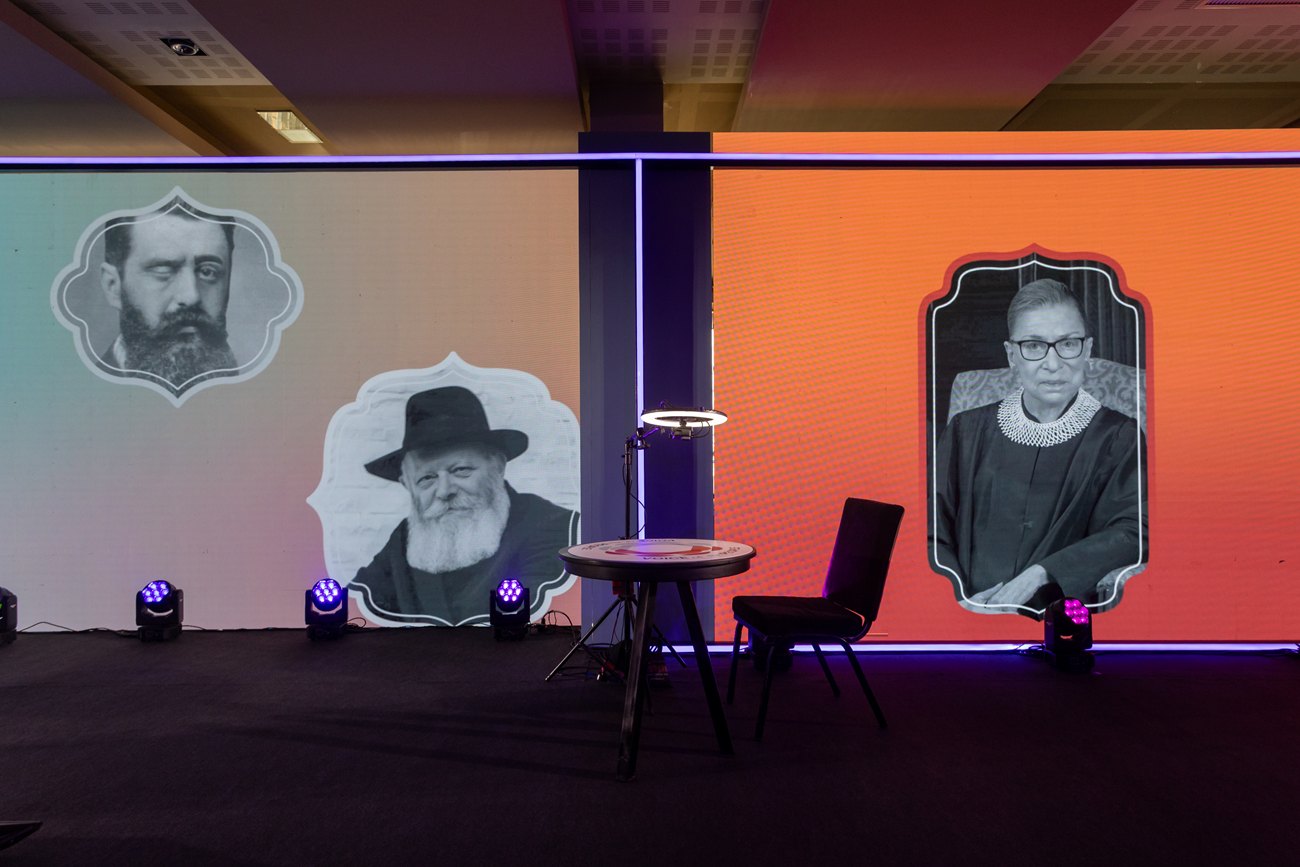 A stage wall built as a lit gallery of portraits, a small round table and a chair set in front of it.